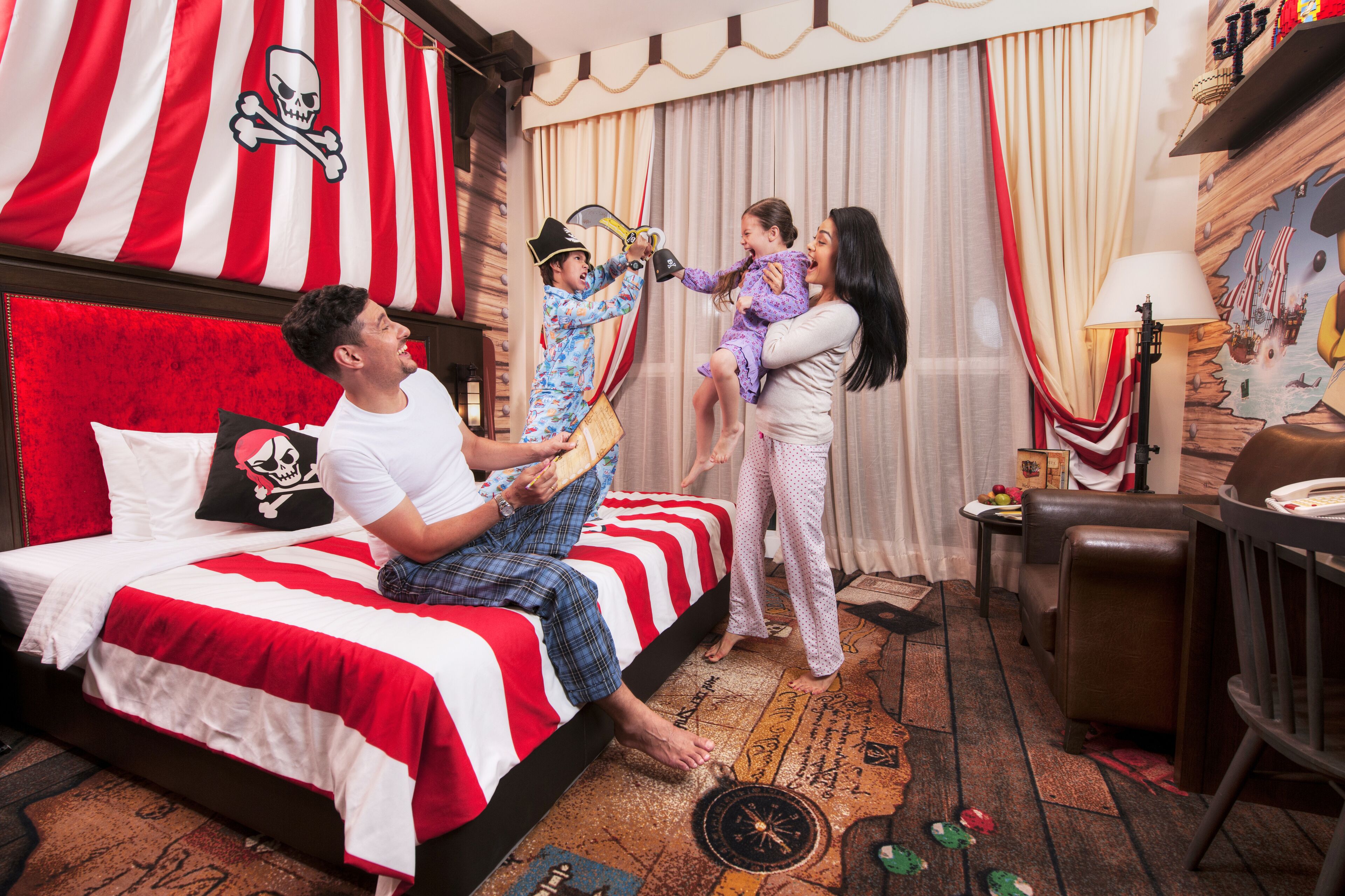 A room with a bed featuring a red and white striped headboard, a skull and crossbones decoration, and a pirate-themed pillow.