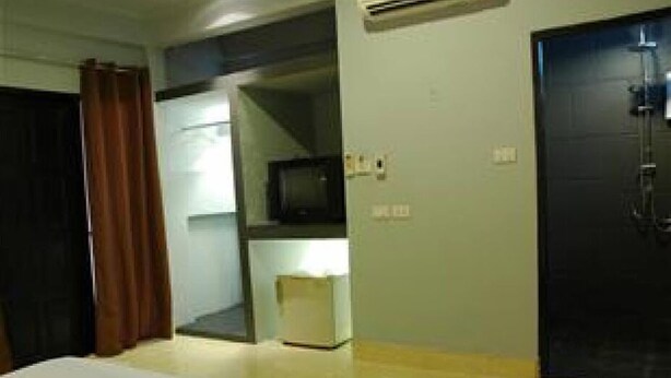 A hotel room with a bed, a television, a small table, and a door. - The Dream Garden (Krabi)