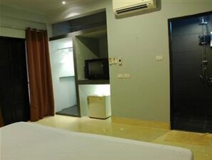 A hotel room with a bed, a television, a small table, and a door. - The Dream Garden (Krabi)