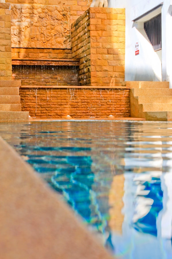 A swimming pool with clear water, a stone wall with a relief sculpture, and a staircase leading up to a door.