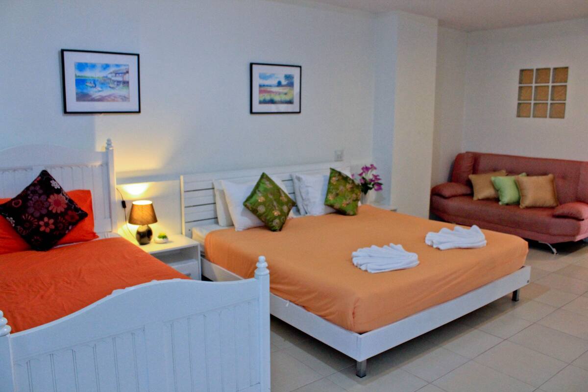 A hotel room with two beds, a sofa, and a small table with a lamp.