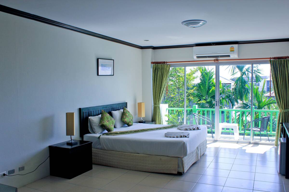 A hotel room with a bed, bedside table, lamp, and an air conditioning unit.