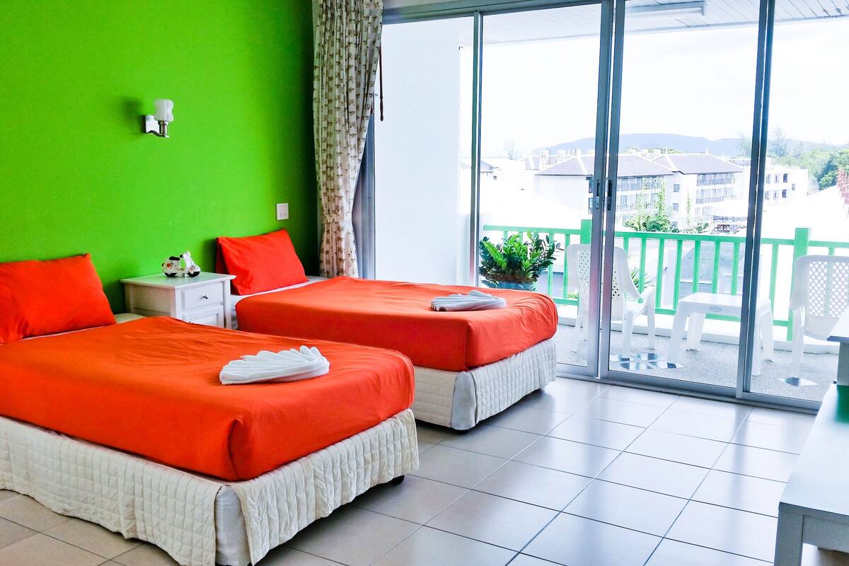A hotel room with two beds, green walls, and a balcony with a view of the city.