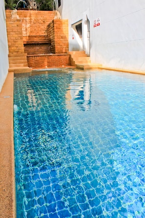 A rectangular swimming pool with clear blue water, surrounded by a brick wall and a white building. - Ben's House (Krabi)