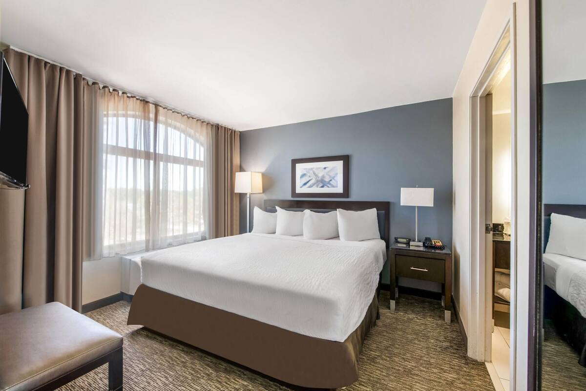 Ein Hotelzimmer mit einem großen Bett, einem Nachttisch mit Lampe, einem kleinen Schreibtisch und einem Sessel.