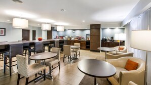A modern hotel lobby with a bar area, seating arrangements, and a kitchen in the background. - Wingate by Wyndham Slidell/New Orleans East Area (Slidell)