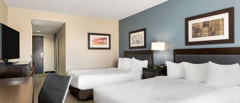 A hotel room with two beds, a desk, a chair, a TV, and framed artwork on the walls.