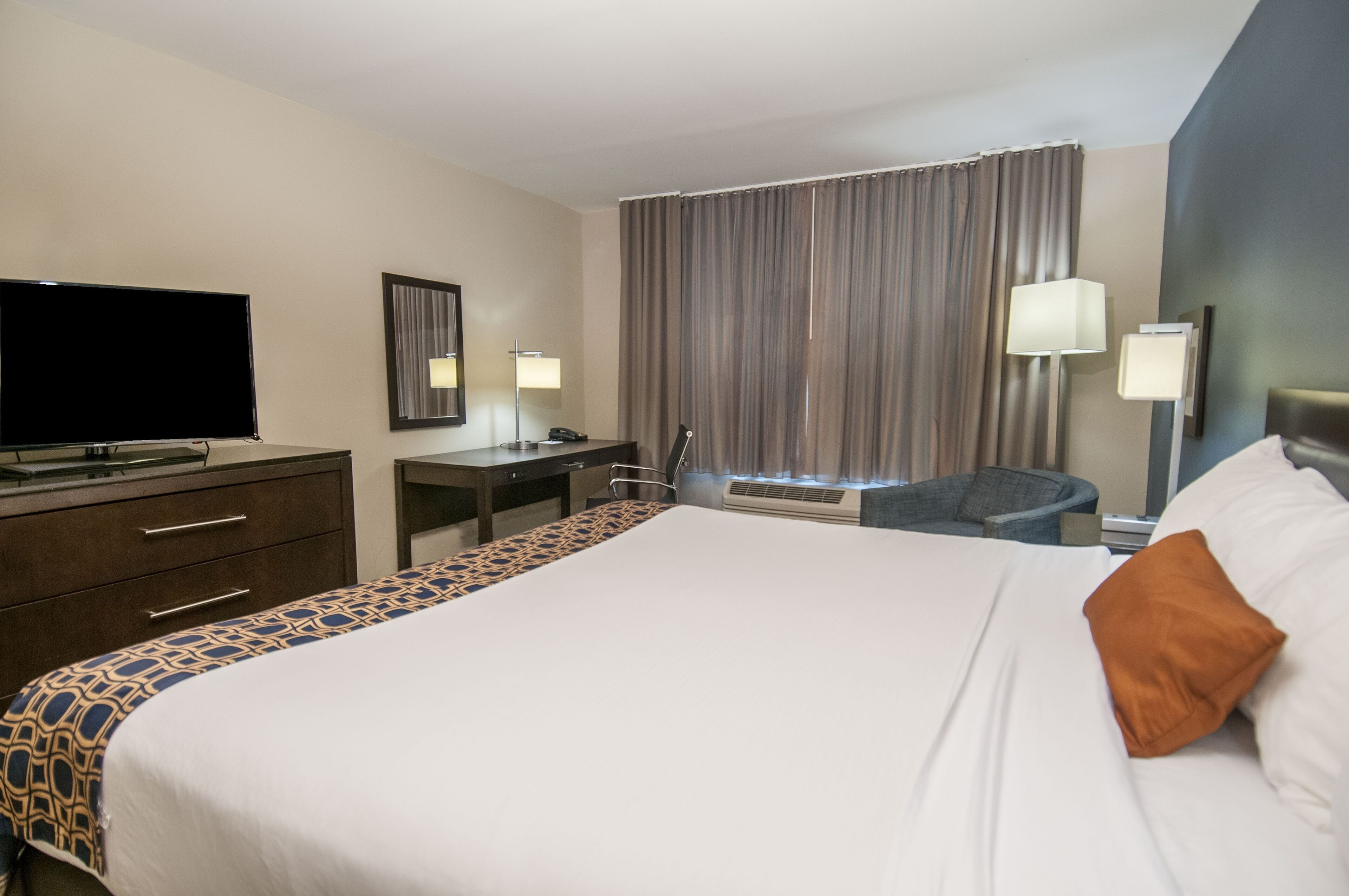 Una habitación de hotel con una cama grande, un escritorio, una silla, un televisor y una ventana con cortinas.