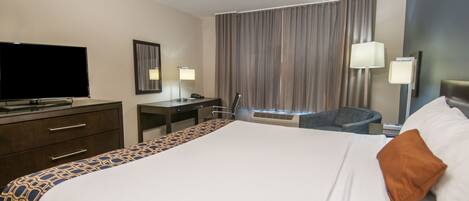 Una habitación de hotel con una cama grande, un escritorio, una silla, un televisor y una ventana con cortinas.