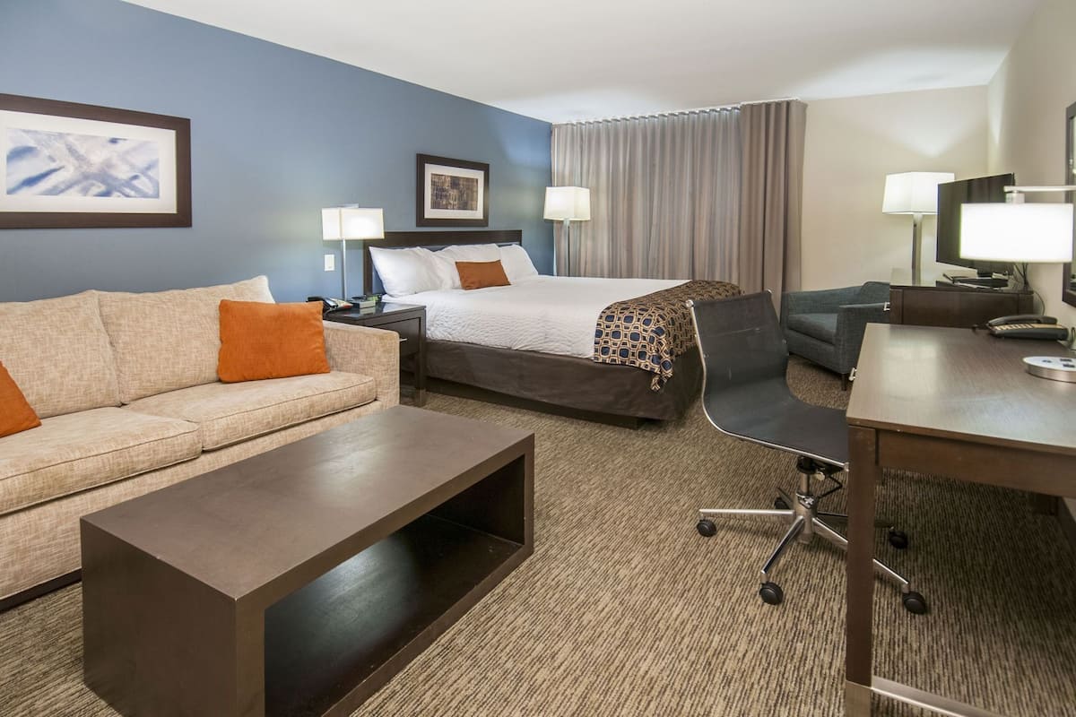 Ein Hotelzimmer mit Bett, Sofa, Schreibtisch, Sessel und zwei Lampen.