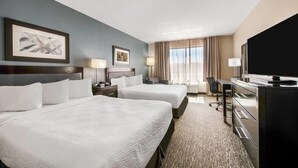 A hotel room with two beds, a desk, a television, and a large window with curtains. - Wingate by Wyndham Slidell/New Orleans East Area (Slidell)