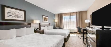 A hotel room with two beds, a desk, a television, and a large window with curtains.