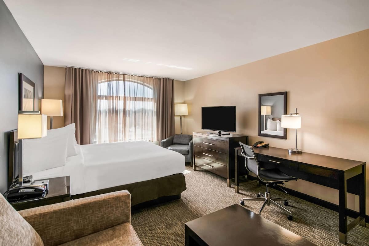 Ein Hotelzimmer mit einem großen Bett, einem Schreibtisch, einem Sessel, einem Fernseher und einer Schreibtischlampe.
