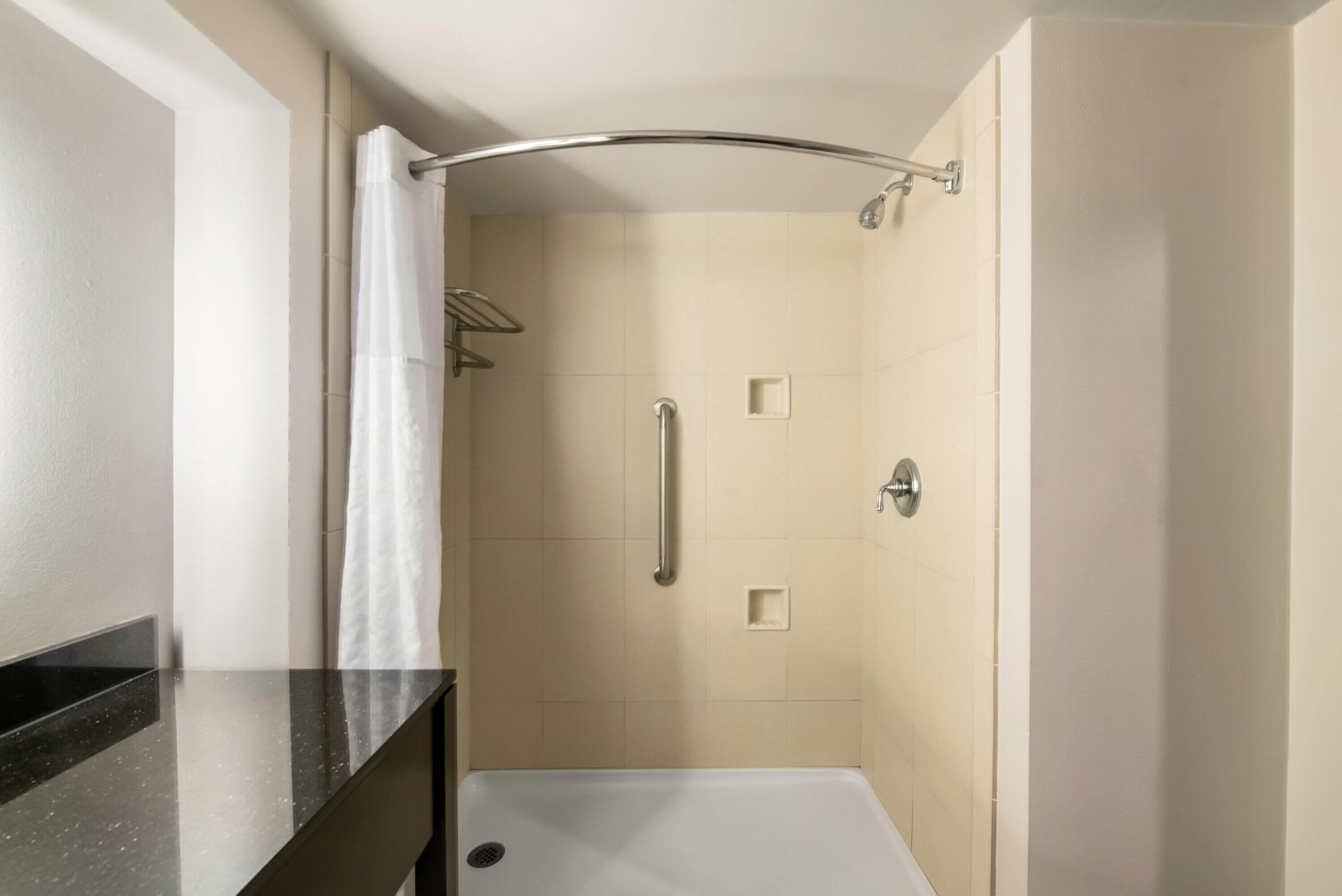 A small, enclosed shower area with a curved showerhead, a handrail, and a white curtain.