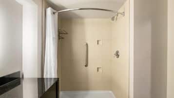 A small, enclosed shower area with a curved showerhead, a handrail, and a white curtain.