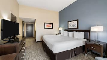 A hotel room with a large bed, a TV, a desk with a lamp, and a framed picture on the wall.