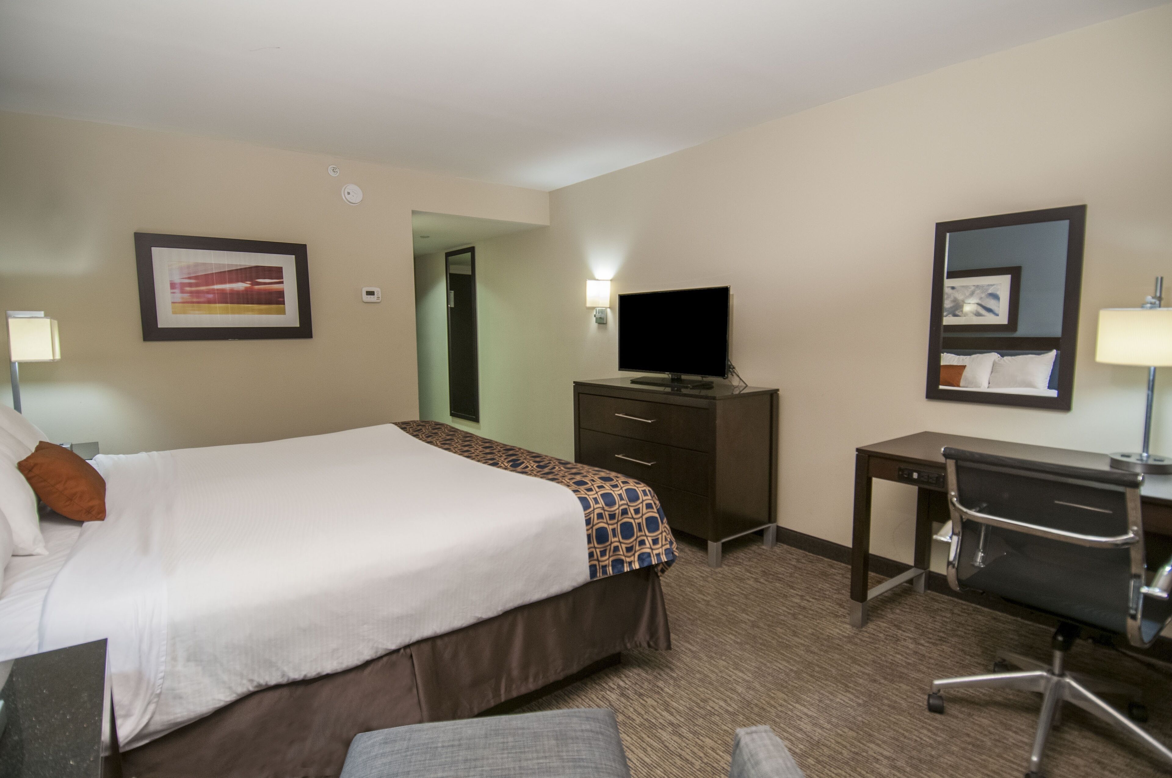 Ein Hotelzimmer mit Bett, Schreibtisch, Stuhl, Fernseher und Spiegel.