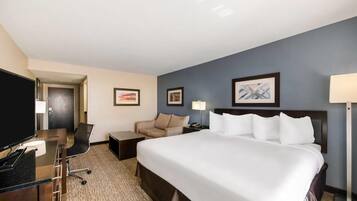 A hotel room with a large bed, a desk with a computer, a chair, a TV, and framed artwork on the wall.
