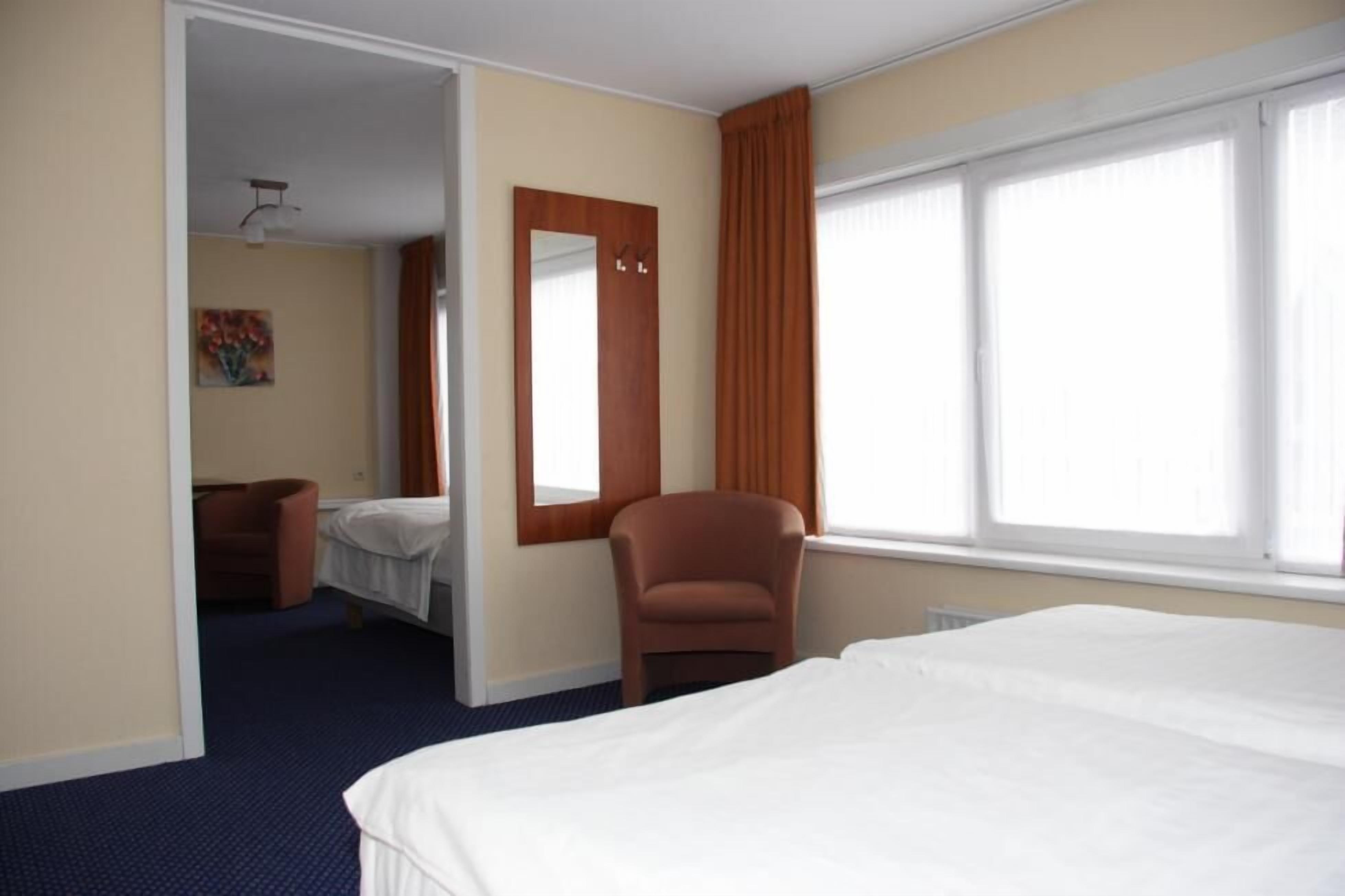 Una habitación de hotel con una cama grande, una silla, un espejo y una ventana.