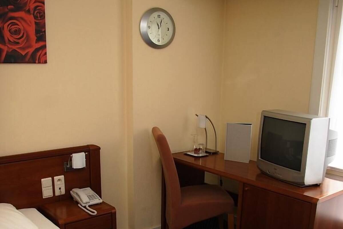 A hotel room with a bed, a desk with a chair, a television, a clock, and a telephone.