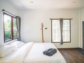 A bedroom with a large bed, two windows, and a wooden floor.