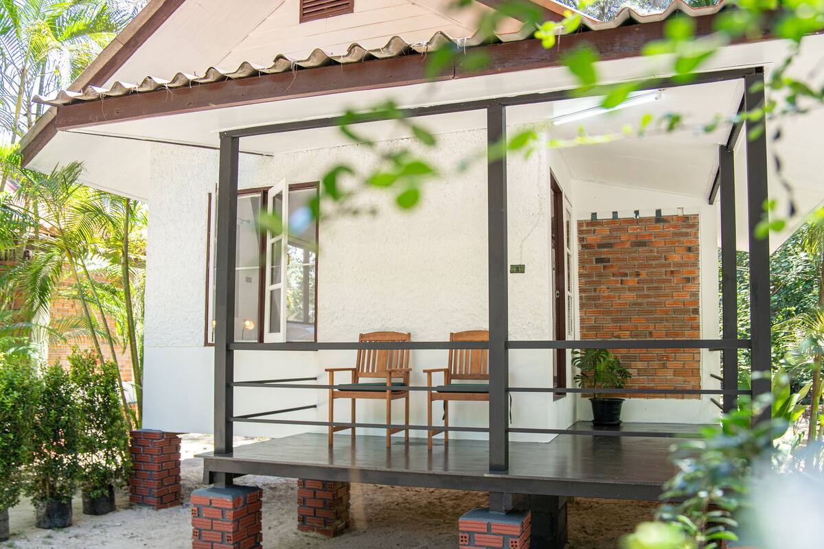 A covered outdoor seating area with a table and chairs, surrounded by potted plants and a brick wall.