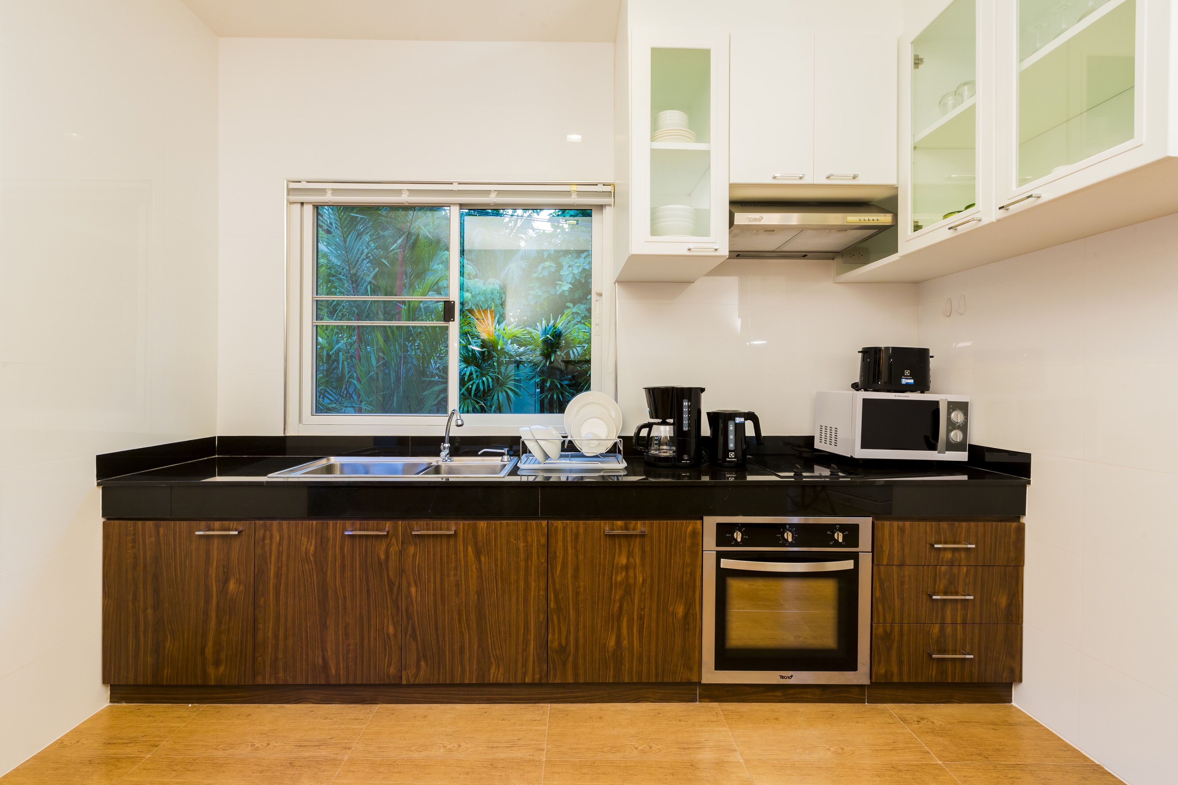 A modern kitchen with a black countertop, wooden cabinets, a built-in oven, a microwave, and a window with a view of greenery.