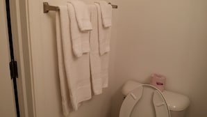 Un baño con inodoro, un perchero con varias toallas blancas y un rollo de papel higiénico en la pared.