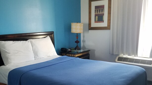 Habitación de hotel con cama, mesita de noche, lámpara, un cuadro en la pared y ventana con cortinas.