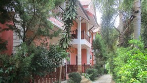 A multi-story building with a red facade, surrounded by lush greenery and a paved pathway. - Lanta Nature House (Ko Lanta)