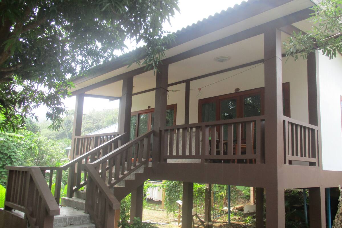 A two-story wooden house with a balcony and a staircase leading to the upper floor.