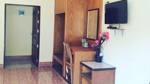 A room with a wooden desk, a chair, a television mounted on the wall, and a door leading to another room. - Phu Lanta Life (Ko Lanta)