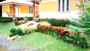 A bungalow-style hotel with a tiled roof, a porch, and a well-maintained garden with red flowers and shrubs. - Phu Lanta Life (Ko Lanta)