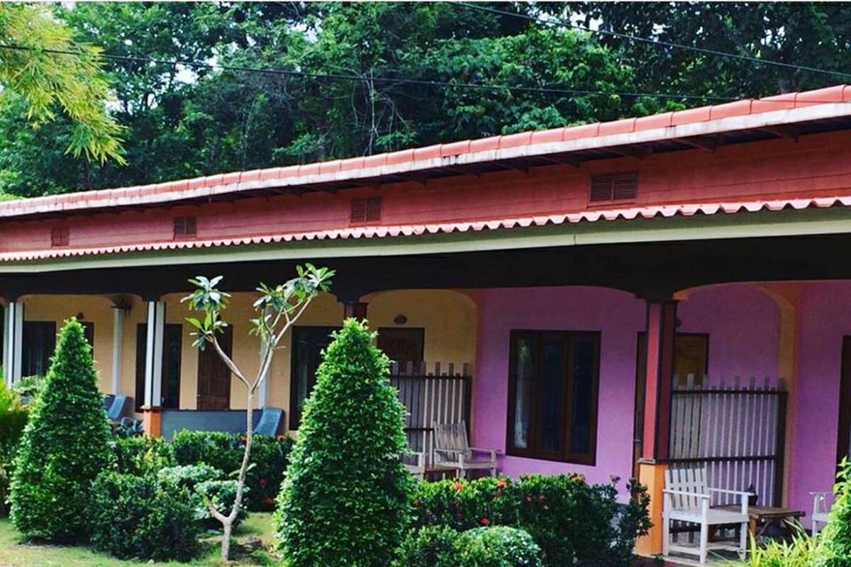 A two-story building with a red roof and a covered porch. There are two small trees in front of the building.