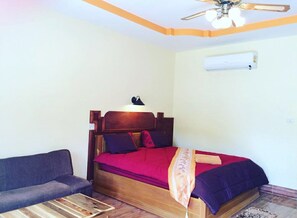 A bedroom with a wooden bed, a red blanket, a grey sofa, and a ceiling fan. - Phu Lanta Life (Ko Lanta)