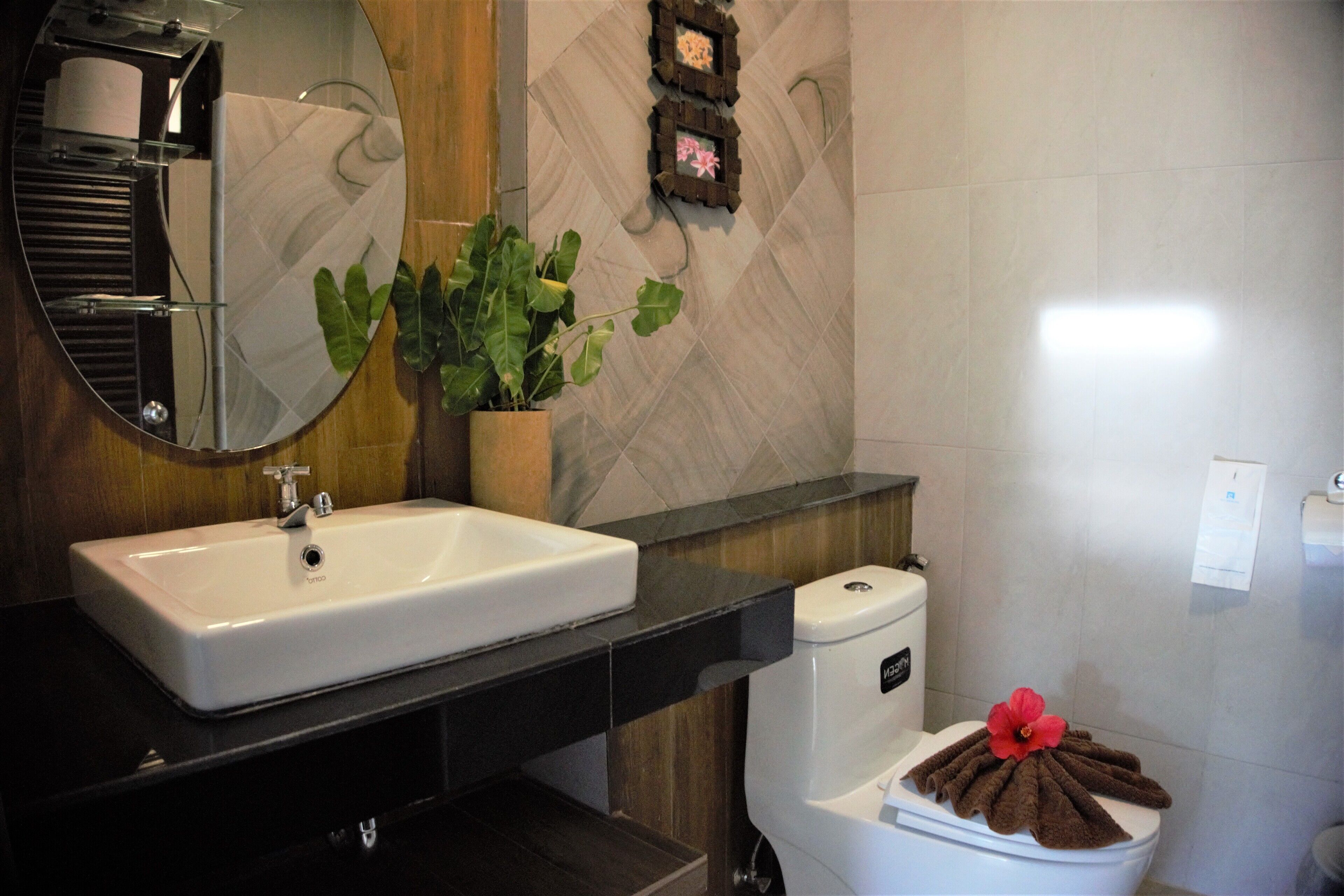 Een badkamer met een wit wastafel, een spiegel, een toilet met een handdoek erop en een potplant.