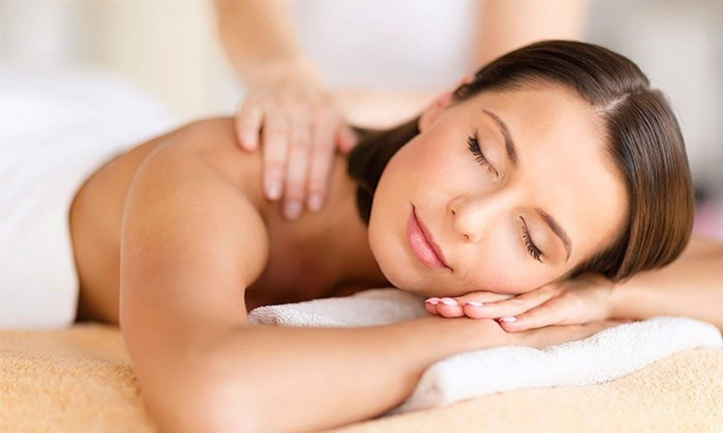 A person lying on a massage table with a towel, receiving a back massage.