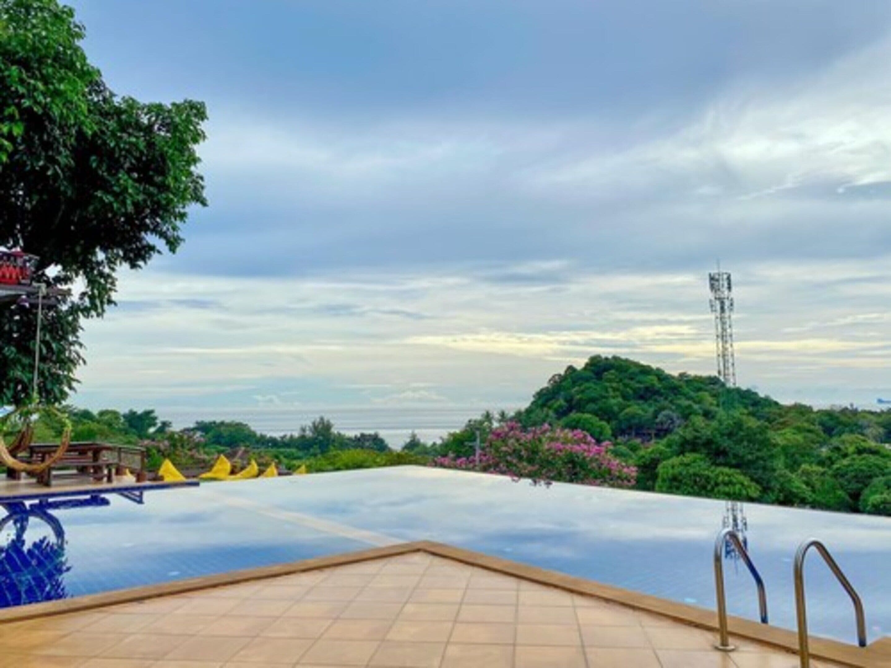 An infinity pool with a view of a lush green landscape and a communication tower in the distance.