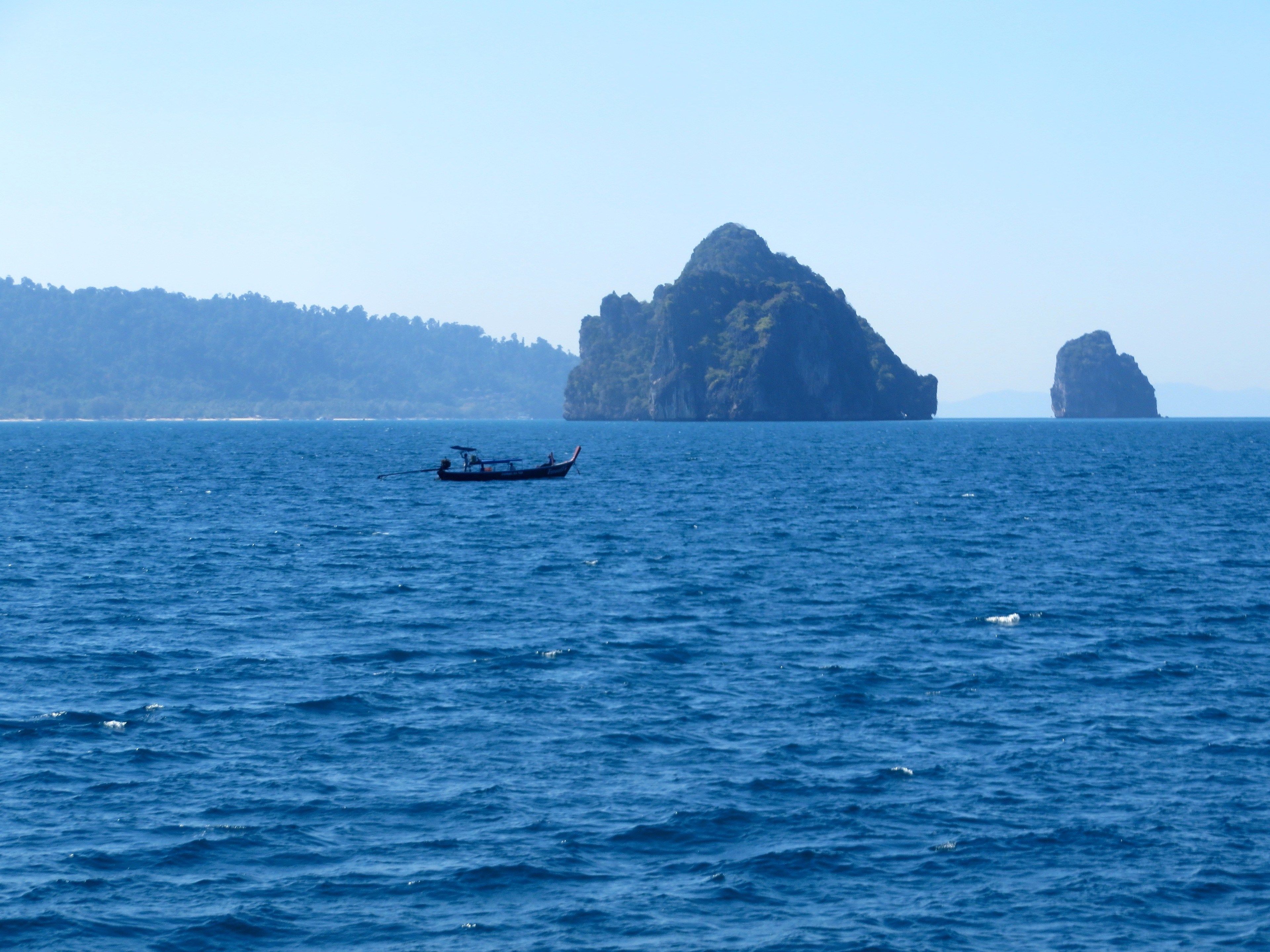 Un barco en agua marina tranquila con una gran formación rocosa al fondo.