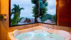 Une grande baignoire ovale, d’où l’on peut admirer un paysage tropical à travers une fenêtre.