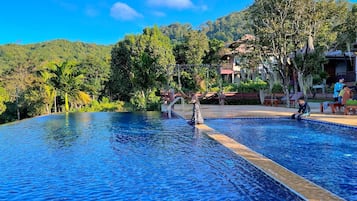 Relax by the serene pool surrounded by lush greenery and traditional-style buildings.