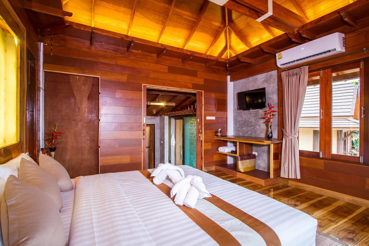 Een kamer met houten lambrisering, een bed, een televisie en een zichtbare badkamer door een geopende deur.