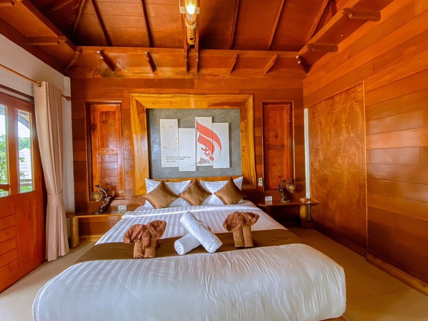 Ein Zimmer aus Holz mit einem Bett, einem gerahmten Bild an der Wand und einem Fenster mit Vorhängen.