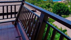 Une terrasse en bois dotée d’une balustrade en verre, offrant une vue sur un paysage côtier.
