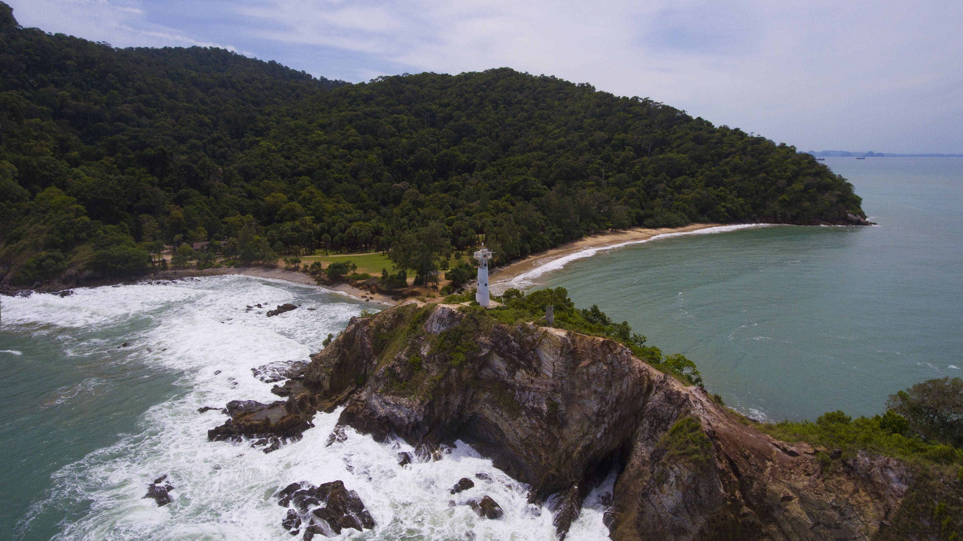 Un paisaje costero con un faro sobre un promontorio rocoso, rodeado de un bosque denso y una playa.