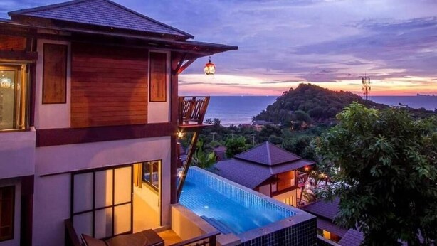 Un hôtel moderne doté d’une piscine, d’une façade en bois et offrant une vue sur l’océan au coucher du soleil.