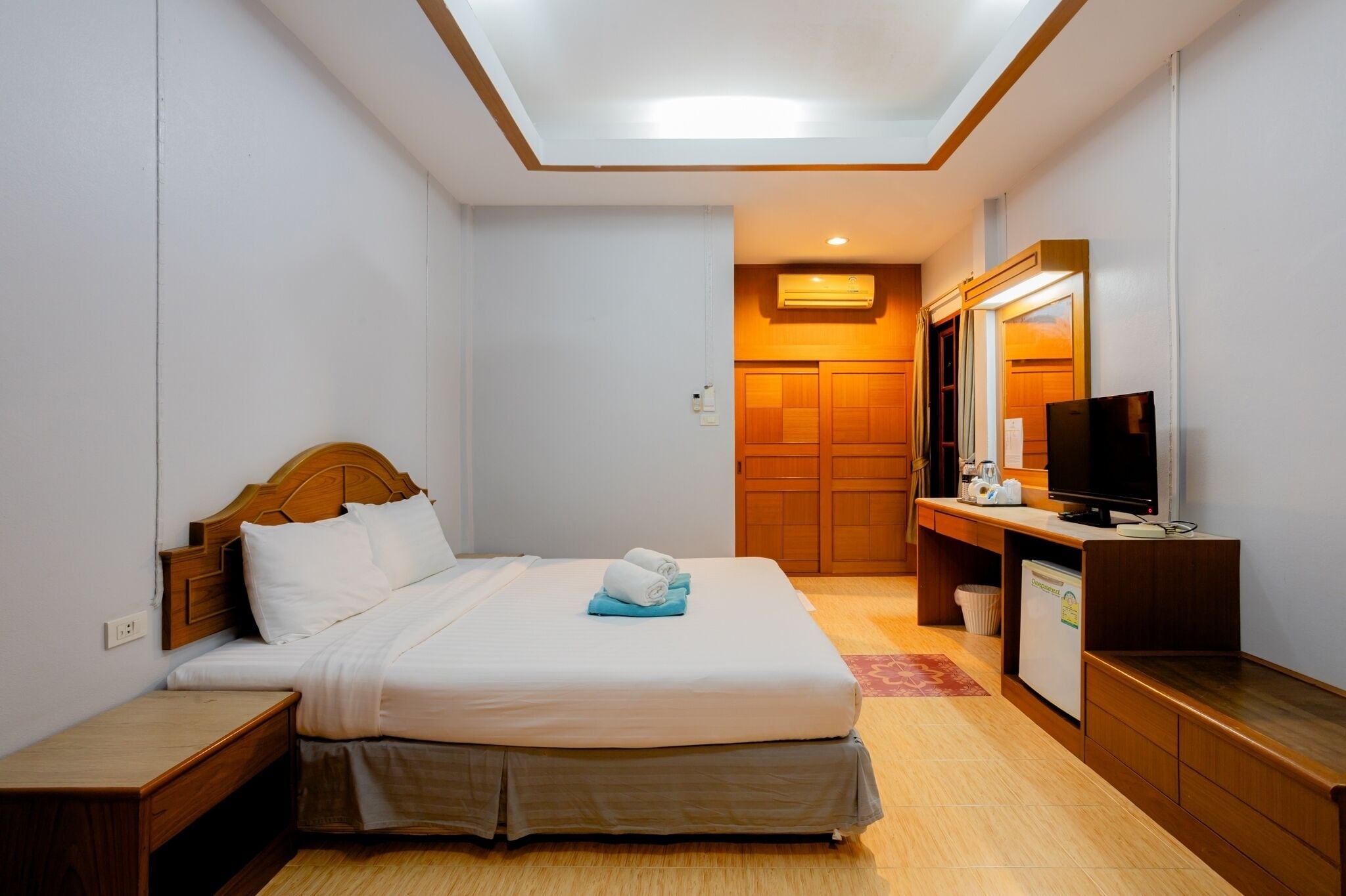 A hotel room with a bed, bedside table, TV, and a wooden wardrobe.