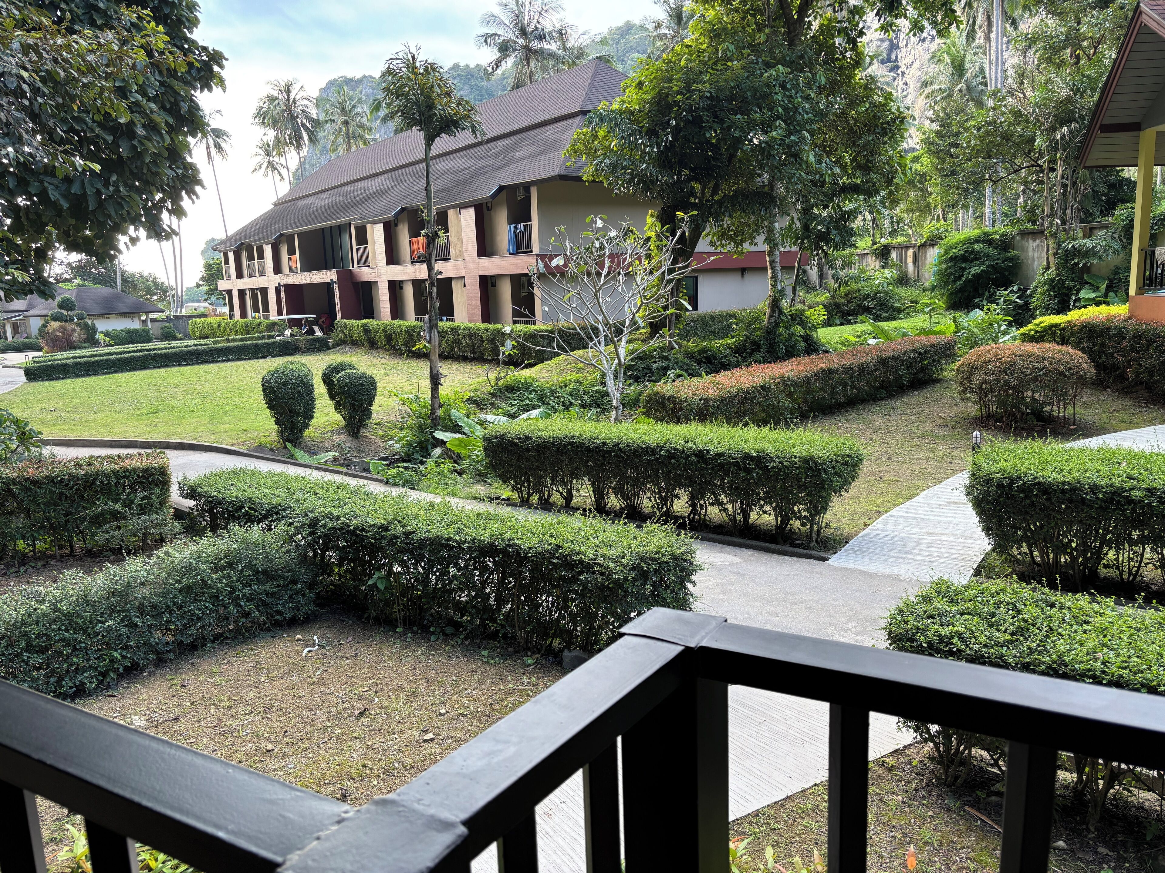 A well-maintained garden with neatly trimmed hedges, a pathway, and a building with multiple balconies.