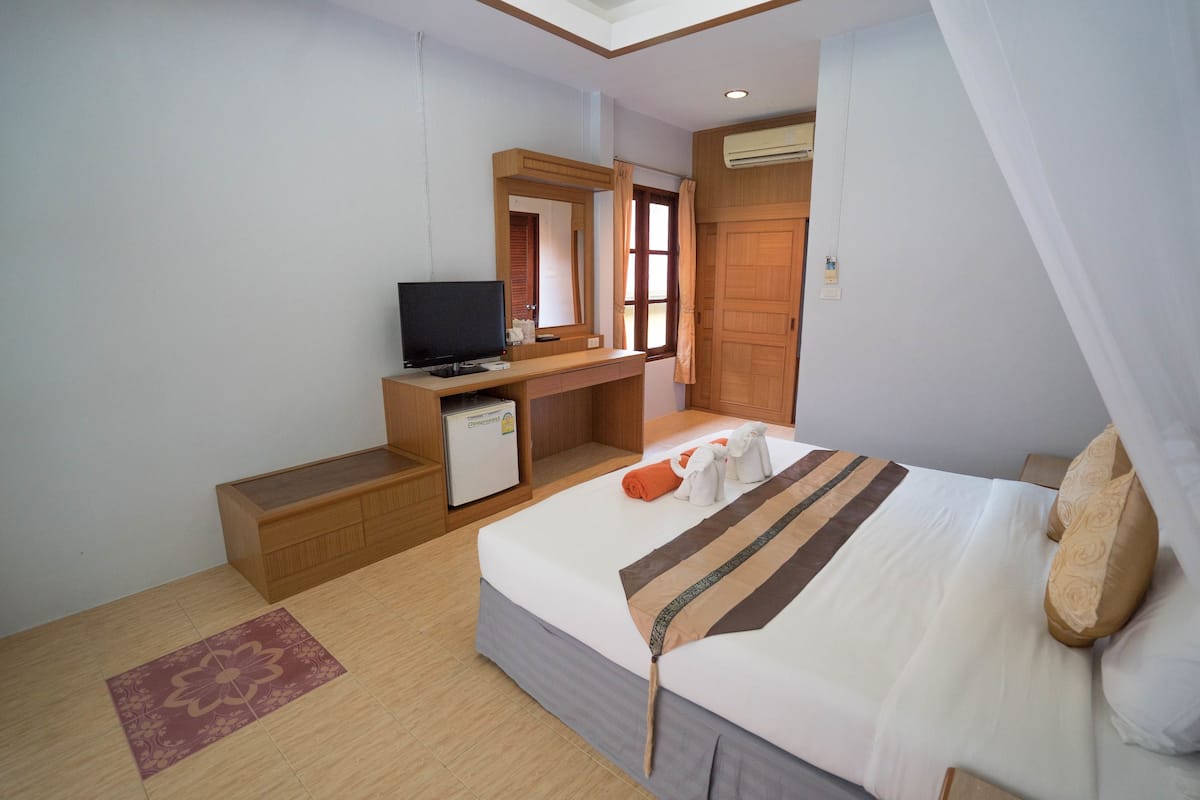 Habitación de hotel con cama, escritorio con televisor, refrigerador pequeño y ventana con cortinas.