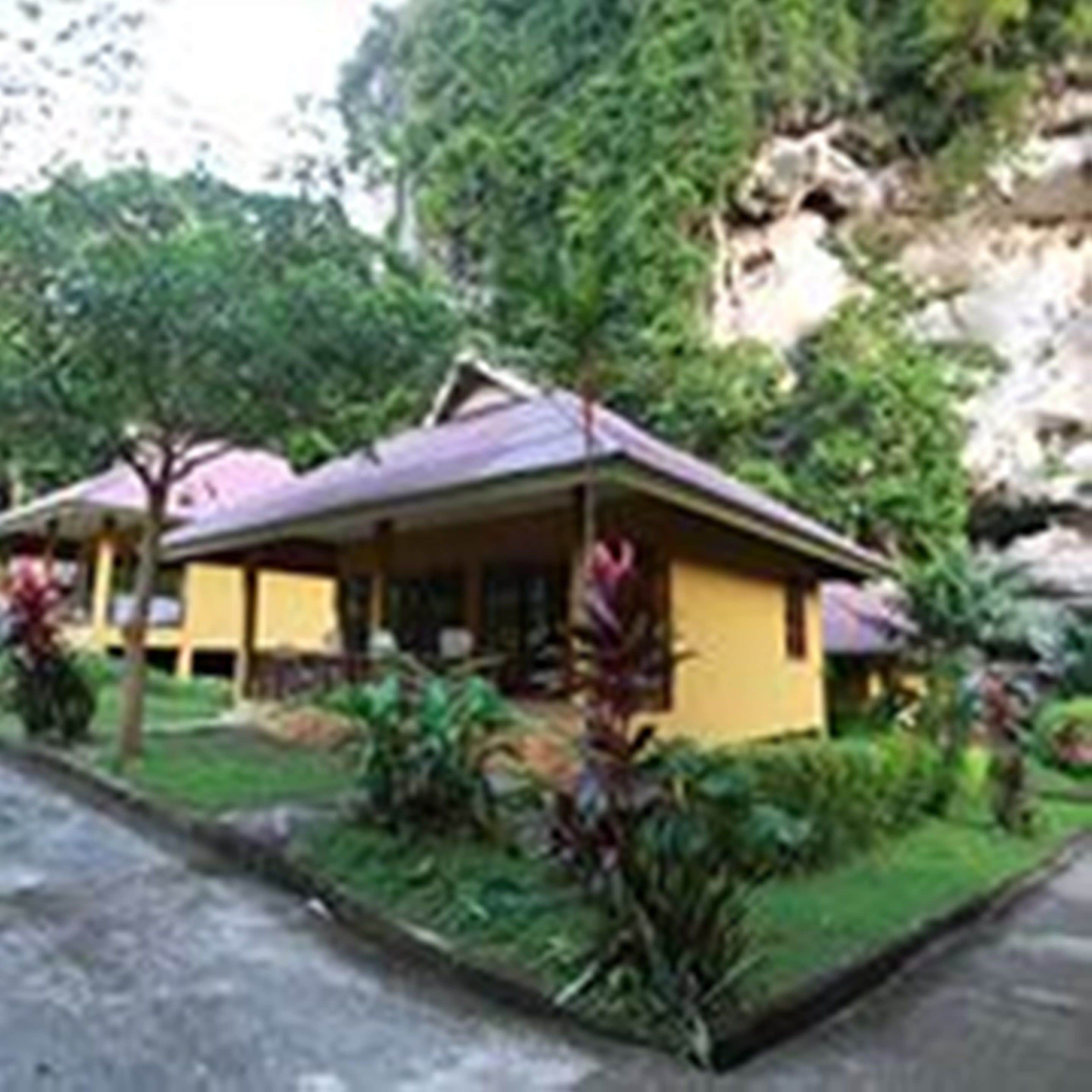 Un hôtel de style bungalow, composé d’un seul bâtiment, entouré d’une végétation luxuriante et bordé d’une falaise rocheuse.